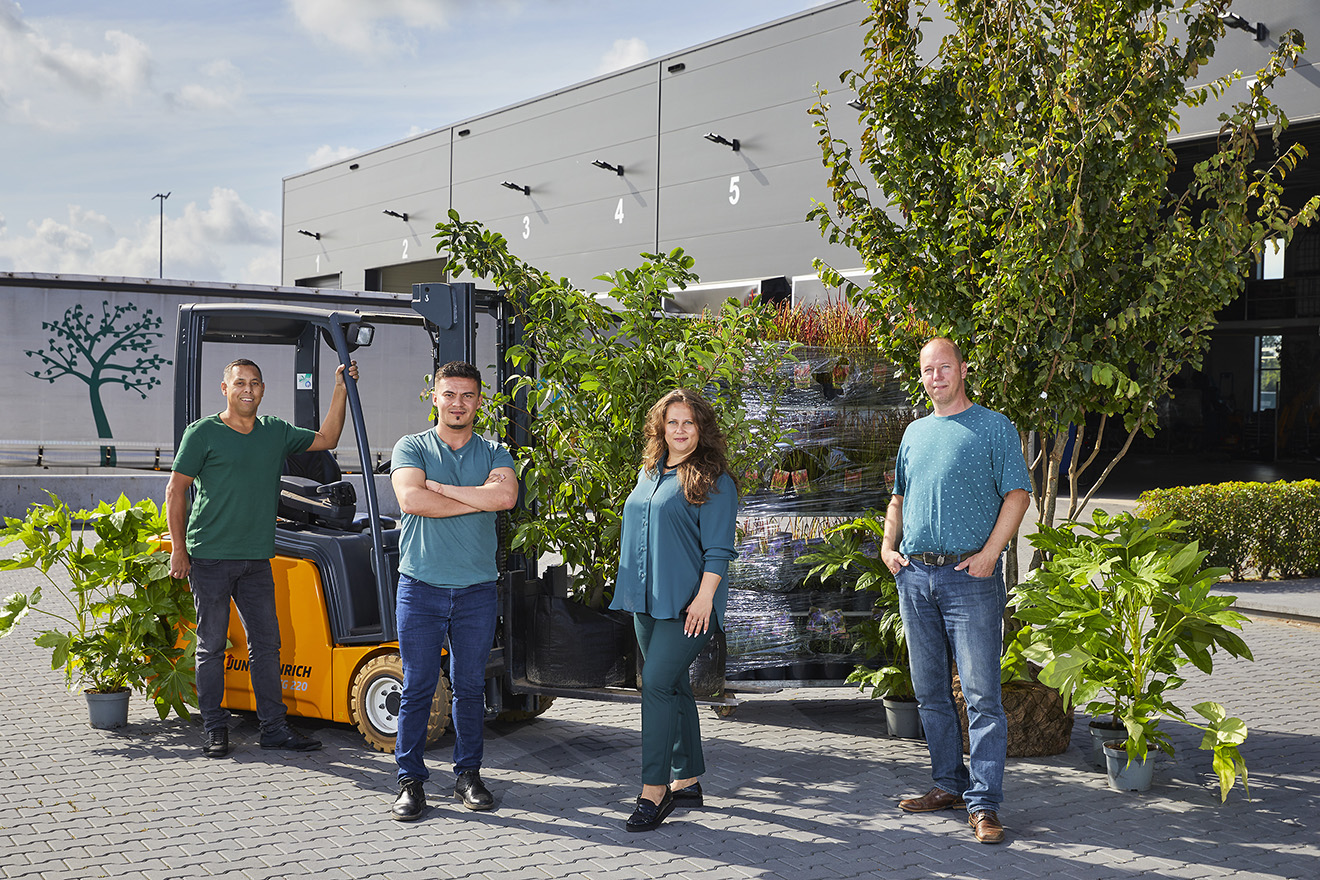 Agro-NL Consult Solutions team met sierplanten klaar voor export, staand naast een vorkheftruck bij een modern magazijn.